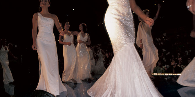 women in white gowns walk the runway